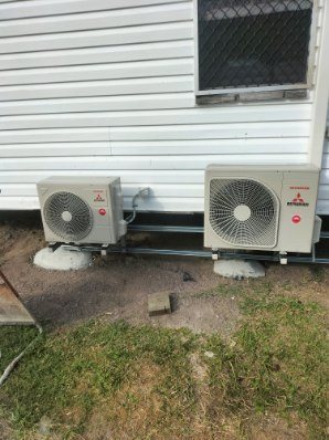 Two Mitsubishi Heavy Industries outdoor units on stands under a weatherboard house