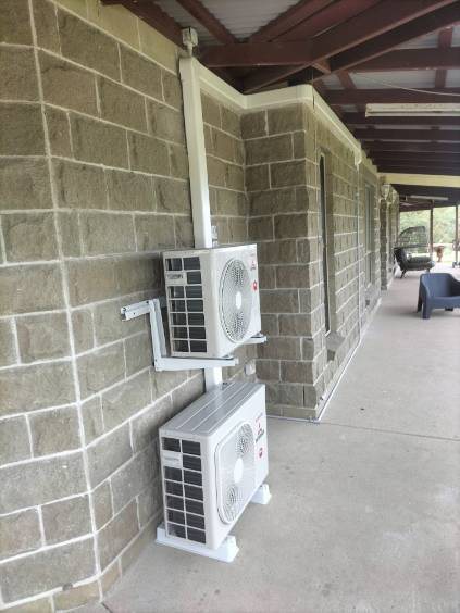 Two Mitsubishi Heavy Industries units stacked on a block wall under a veranda